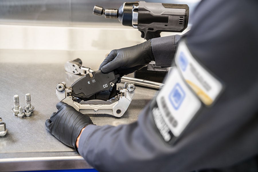 Technician fitting a brake pad into a caliper bracket on a workbench